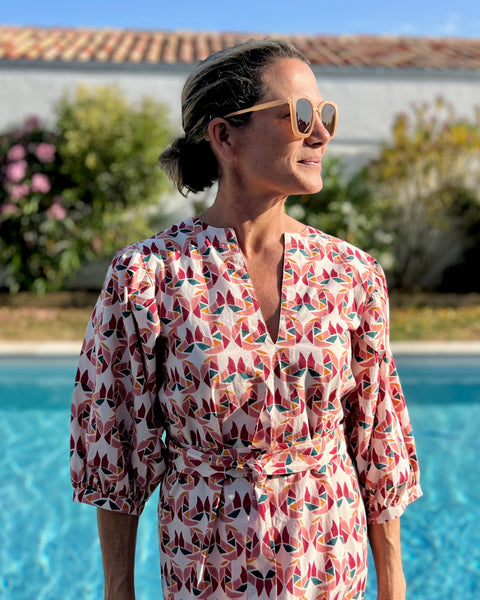 Woman in a patterned puff sleeve dress standing by a pool with flowers and a building in the background
