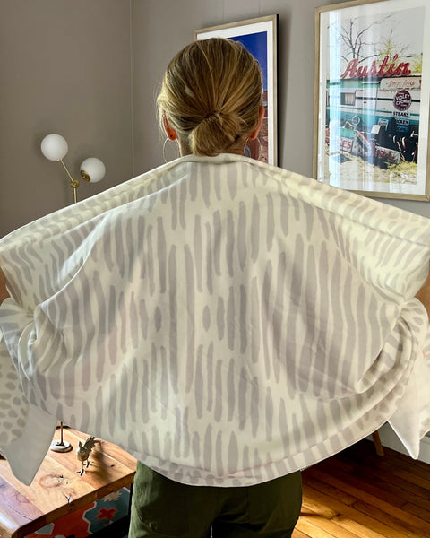 Woman wearing a white and light gray owl print wrap over green pants in a living room