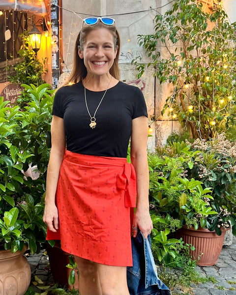 A person wearing a red wrap skirt with a purple block-printed pattern, paired with a black top, standing next to a cafe in Rome