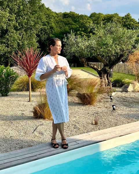 A woman by a pool wearing a white puff sleeve dress with blue print