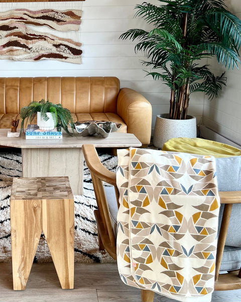 A chair with a cream-colored cozy wrap/scarf with a geometric pattern featuring mustard yellow, taupe, and gray blue