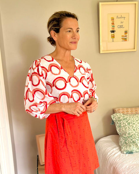 A person wearing a red wrap skirt with a purple block-printed pattern, paired with a block printed white, red, and coral top
