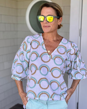 A woman standing outdoors wearing sunglasses and a mint green blouse with puff sleeves, featuring a geometric pattern.