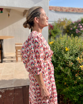 Woman in a multi-colored block printed puff sleeve dress standing outdoors near a pool with greenery and a building in the background.