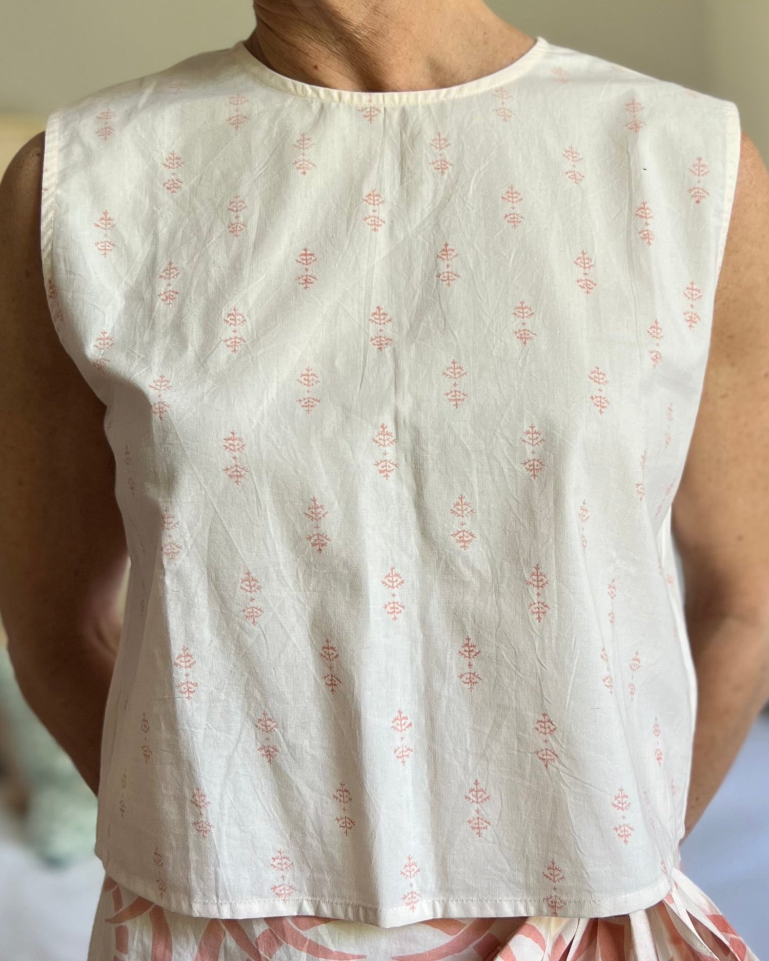 A person wearing a pale peach sleeveless boxy top with a crew neck, paired with a long wrap skirt