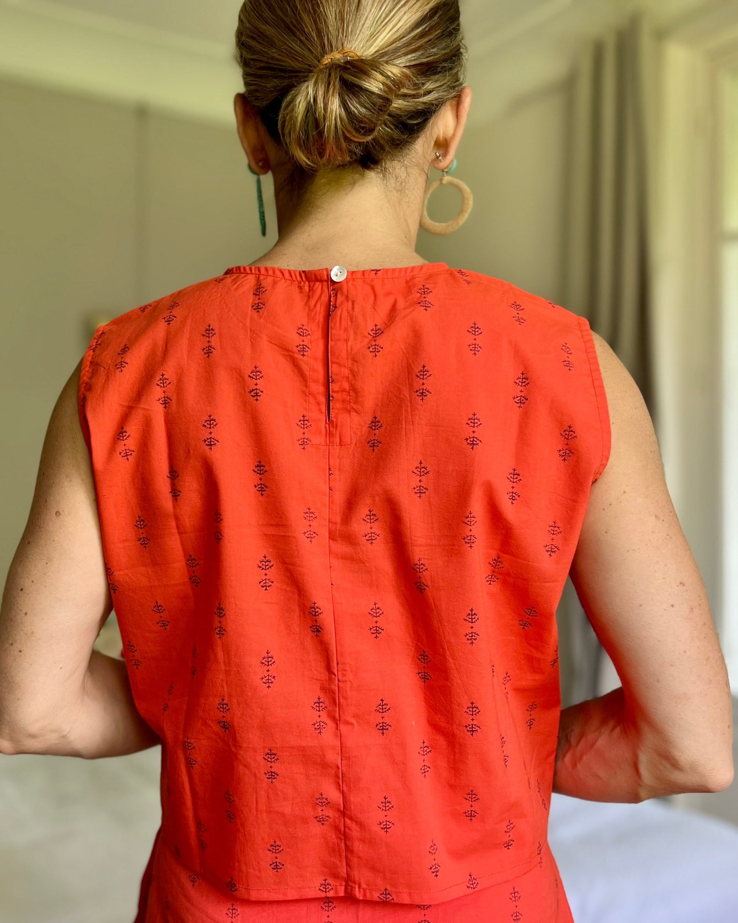 Back of woman wearing tomato red boxy top with button closure at neck