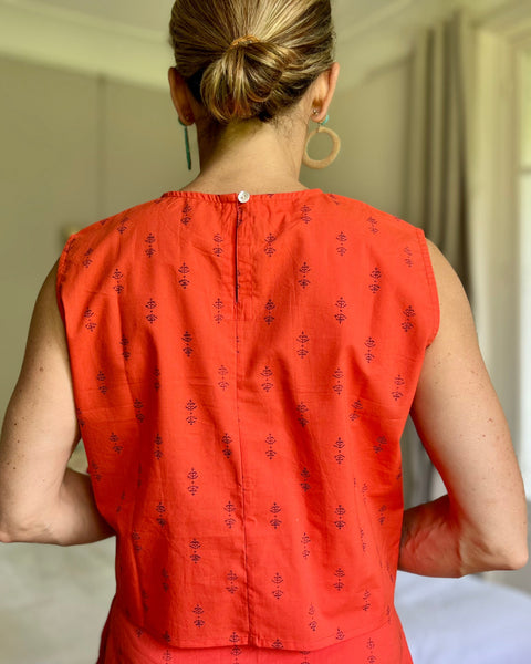 Back of woman wearing tomato red boxy top with button closure at neck