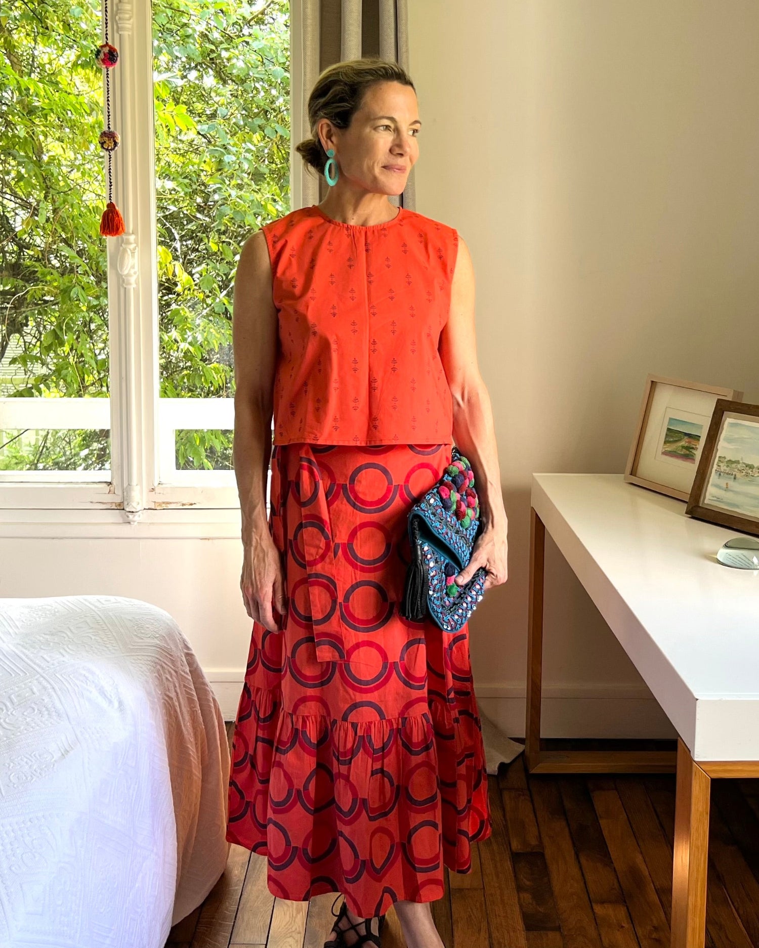 A person wearing a sleeveless, red and purple print, boxy top with a crew neck and a red block printed wrap skirt with a ruffle.