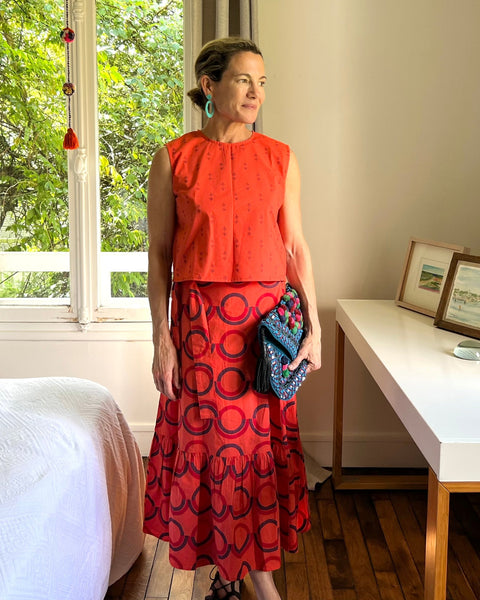 A person wearing a sleeveless, red and purple print, boxy top with a crew neck and a red block printed wrap skirt with a ruffle.
