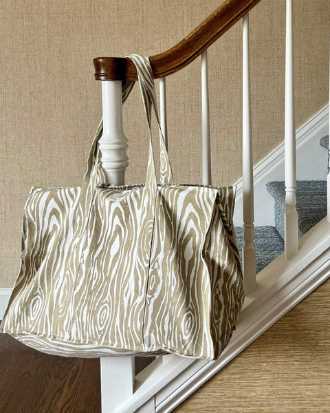 A beige and white faux bois pattern tote bag placed on a bannister.