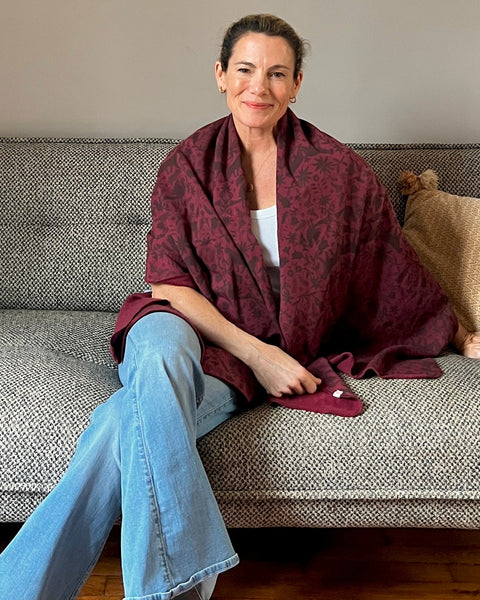 A person sitting on a couch wearing a wine-colored cozy wrap with a brown jaguar print.
