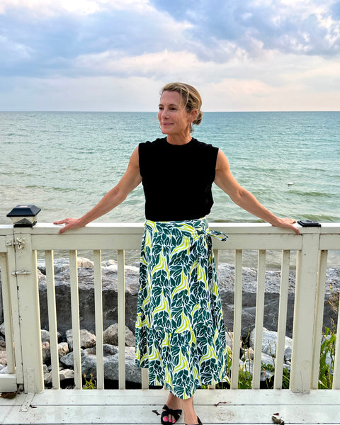 A person wearing a chartreuse snake ruffle wrap skirt with a dark teal green and chartreuse print standing on a deck on the water