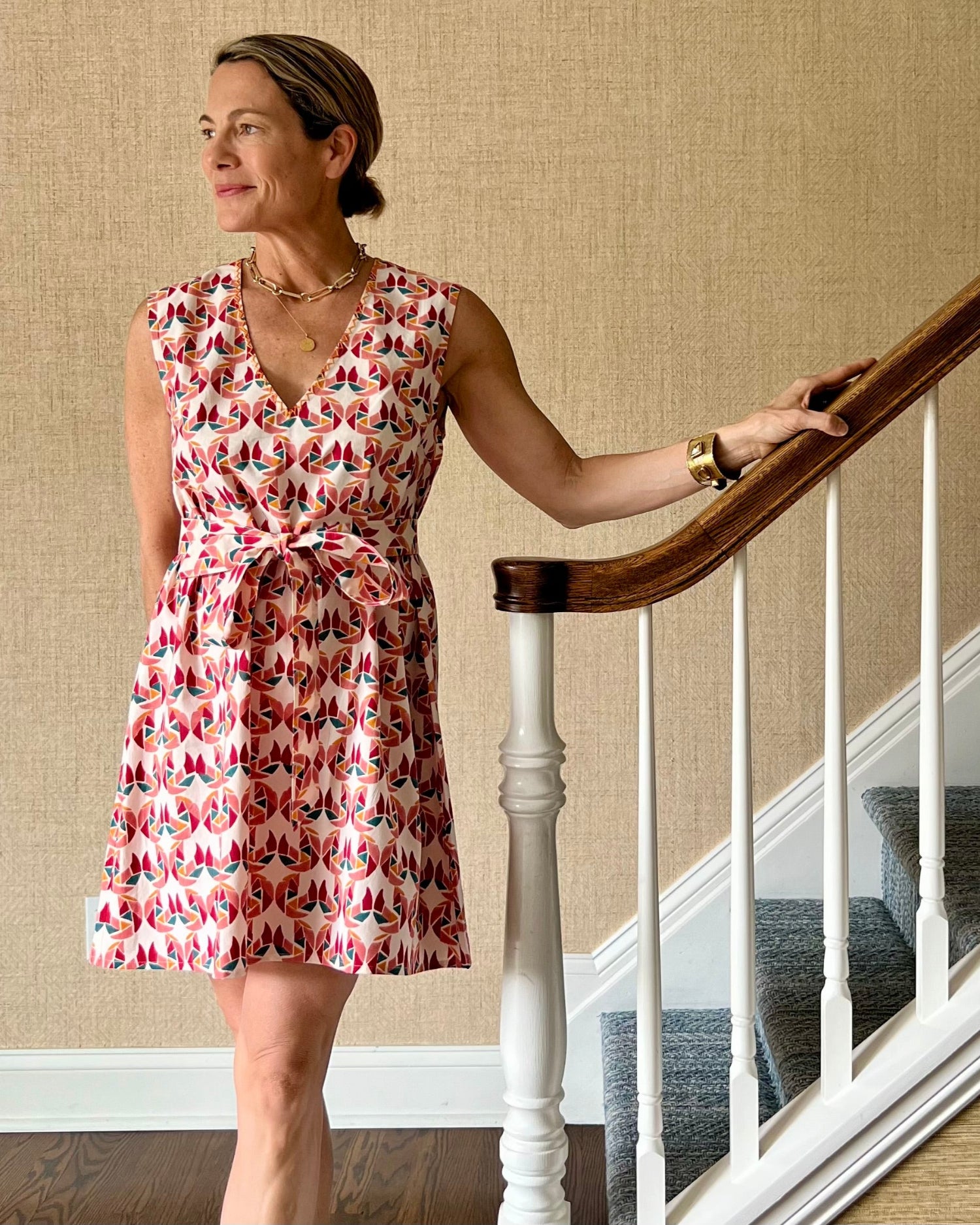 A person wearing a sleeveless, trapeze-shaped summer dress with a confetti mollusk print, standing near a staircase.