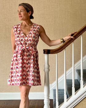 A person wearing a sleeveless, trapeze-shaped summer dress with a confetti mollusk print, standing near a staircase.