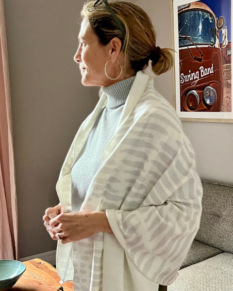 A person standing by a window, wearing a white cozy wrap with a light gray owl print