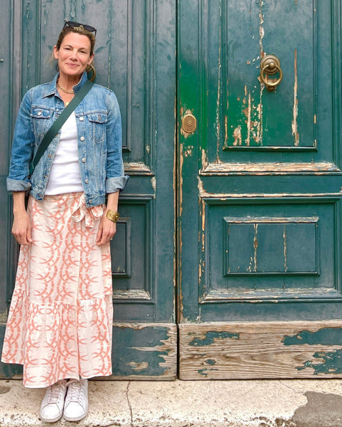 A person wearing a jean jacket, peach-colored wrap skirt with a rhino and horn pattern, and a white top in front of a doorway in Rome