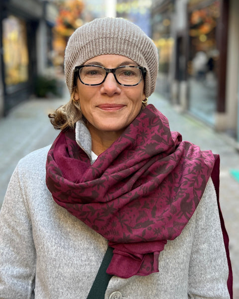 A person with a gray coat and a beret wearing a wine-colored cozy wrap with a brown jaguar print.