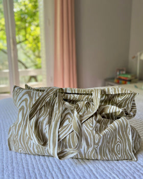 A beige and white faux bois pattern tote bag placed on a bed.