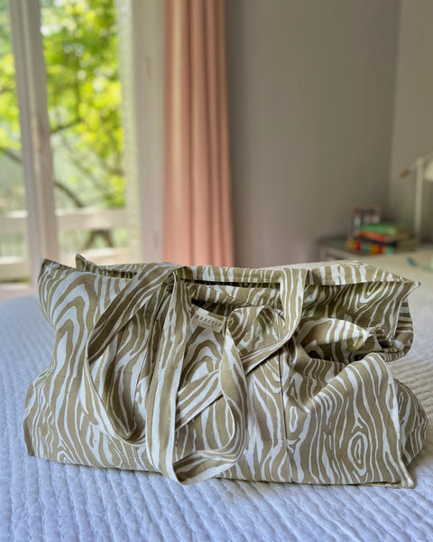 A beige and white faux bois pattern tote bag placed on a bed.