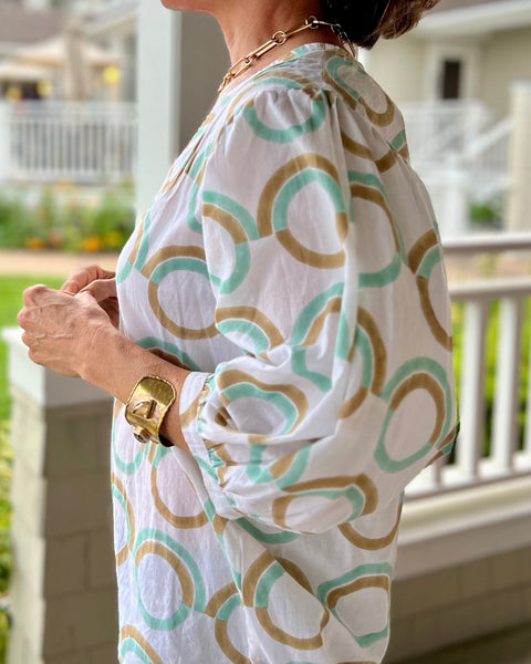 Side view of woman standing outdoors wearing a mint green blouse with puff sleeves, featuring a geometric pattern.