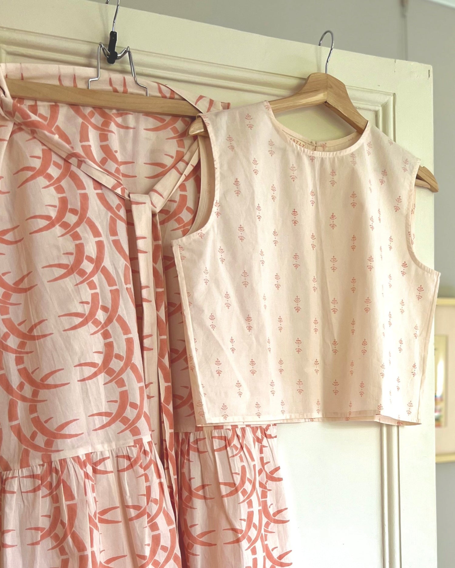 A pale peach sleeveless boxy top with a crew neck, paired with a long wrap skirt on hangers