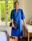A woman standing in a room wearing a royal blue dress with puff sleeves and a V-neck