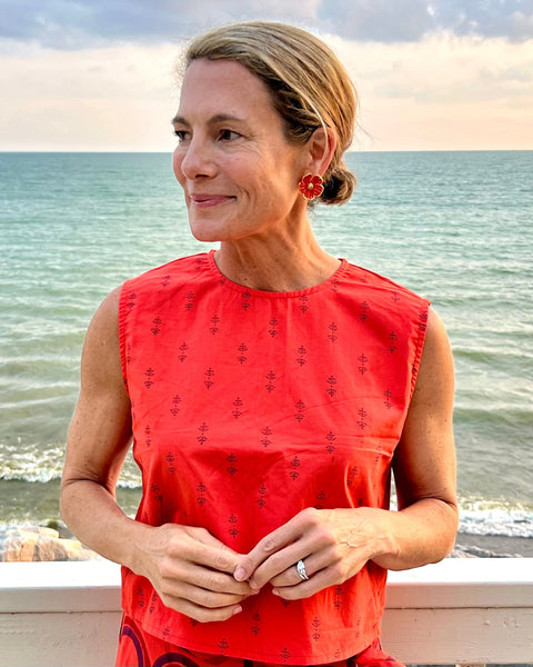 A person wearing a sleeveless, red and purple print, boxy top with a crew neck on the water