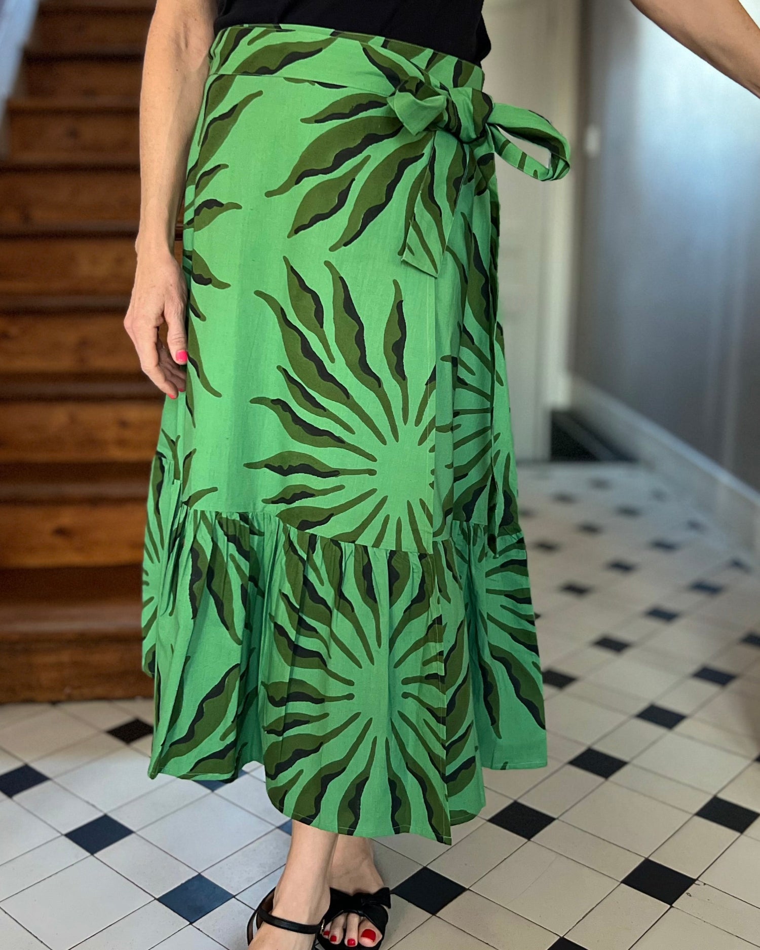 Beautiful green and black block-printed wrap skirt with ruffle and bow on woman in hallway 