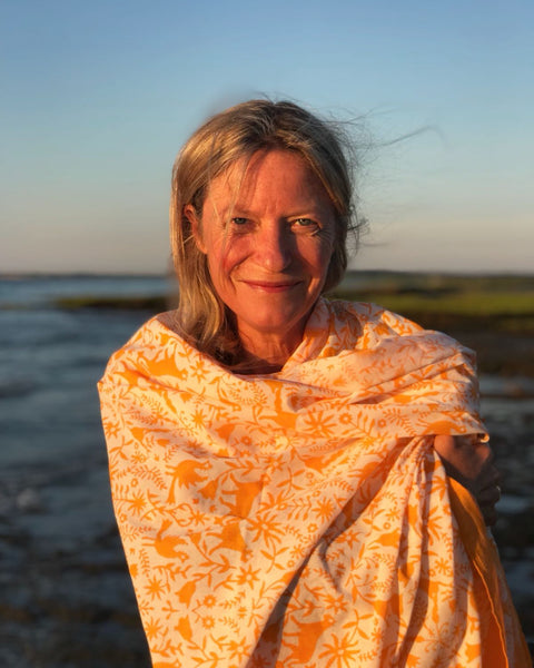 Woman on a beach wrapped up in an orange hand block-printed jaguar sarong / grand scarf with ocean and sunset in the background