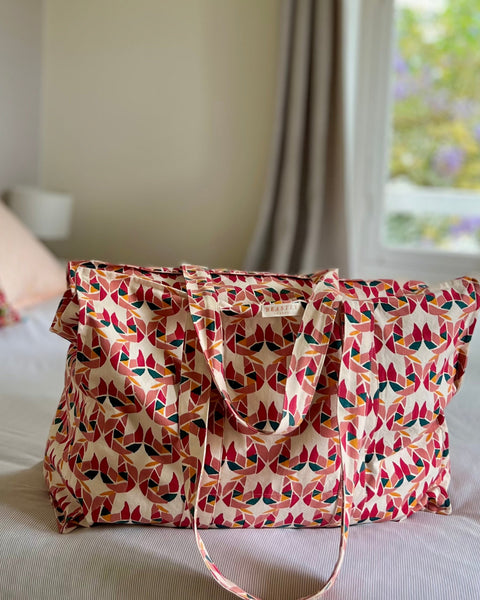 A tote bag with a colorful block-printed pattern featuring mollusks, displayed on a bed.