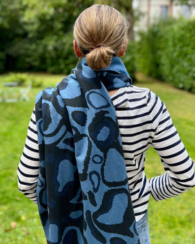 A person wearing a striped shirt with a navy blue and black scarf featuring a wild dog print wrapped around the neck.