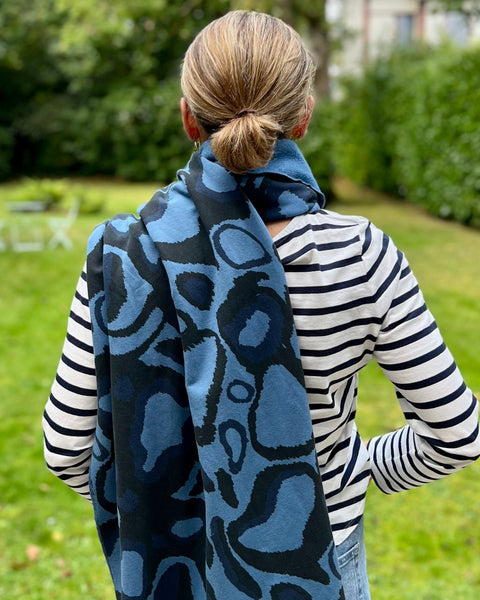 A person wearing a striped shirt with a navy blue and black scarf featuring a wild dog print wrapped around the neck.