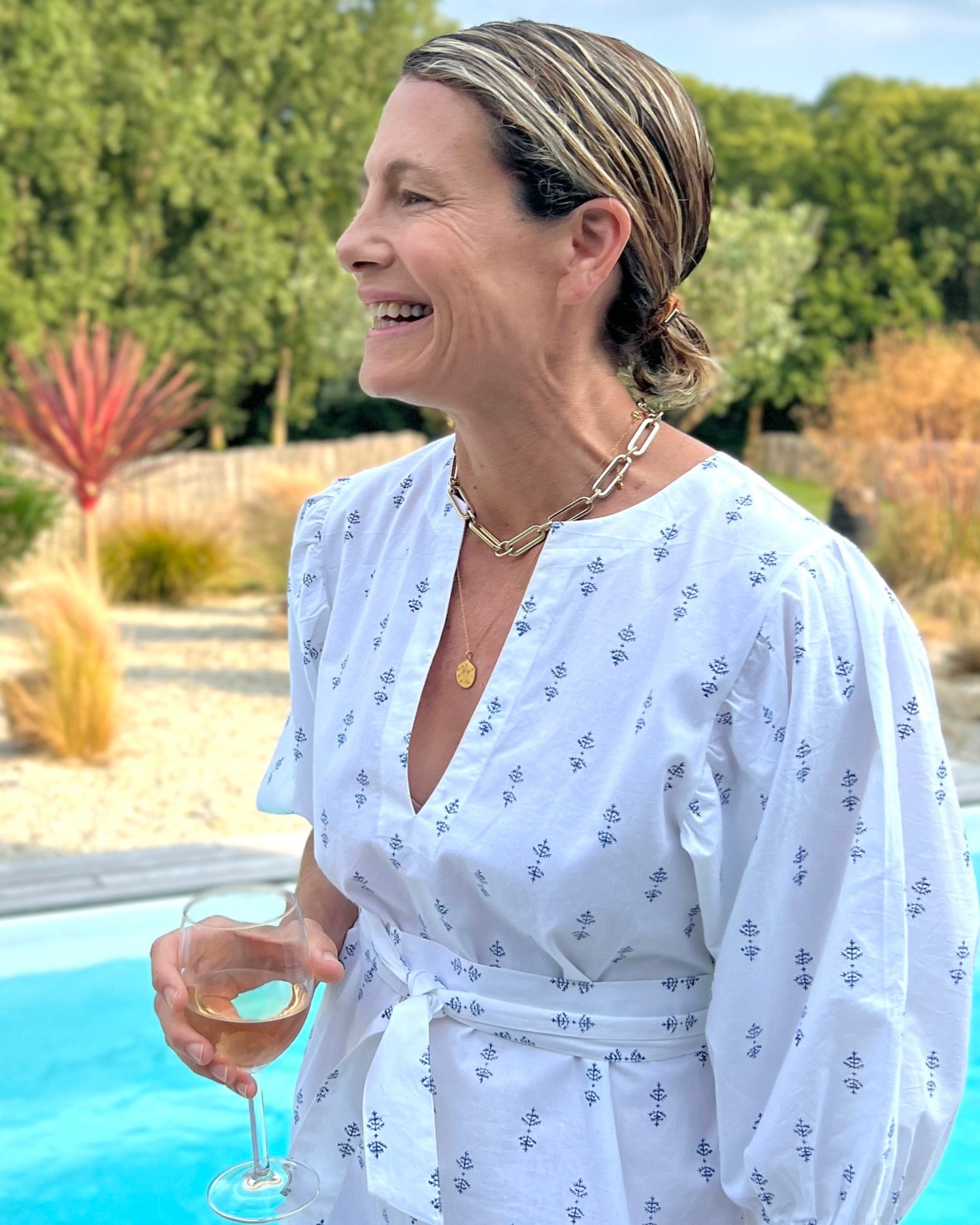 A woman by a pool wearing a white puff sleeve dress with blue print