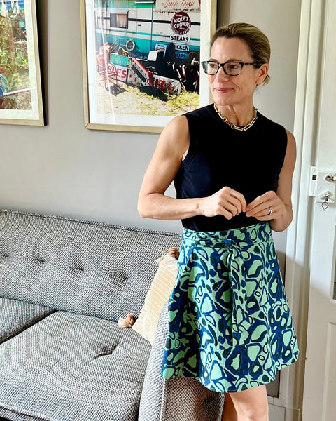 A person wearing a green wrap skirt with an animal print in navy blue, paired with a black top, standing in a room with natural lighting.