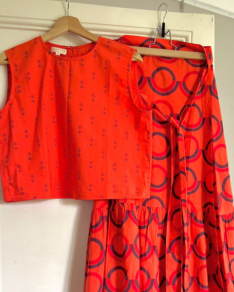A sleeveless, red and purple print, boxy top with a crew neck and a red block printed wrap skirt with a ruffle on hangers