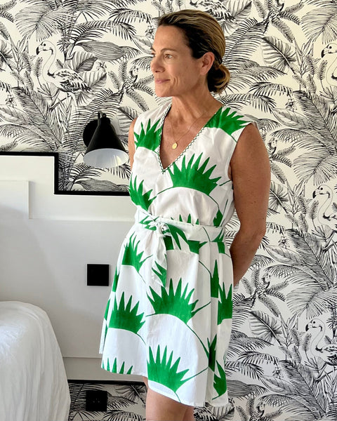 A woman standing in a room with a sleeveless shift dress featuring a grass green print on a white background