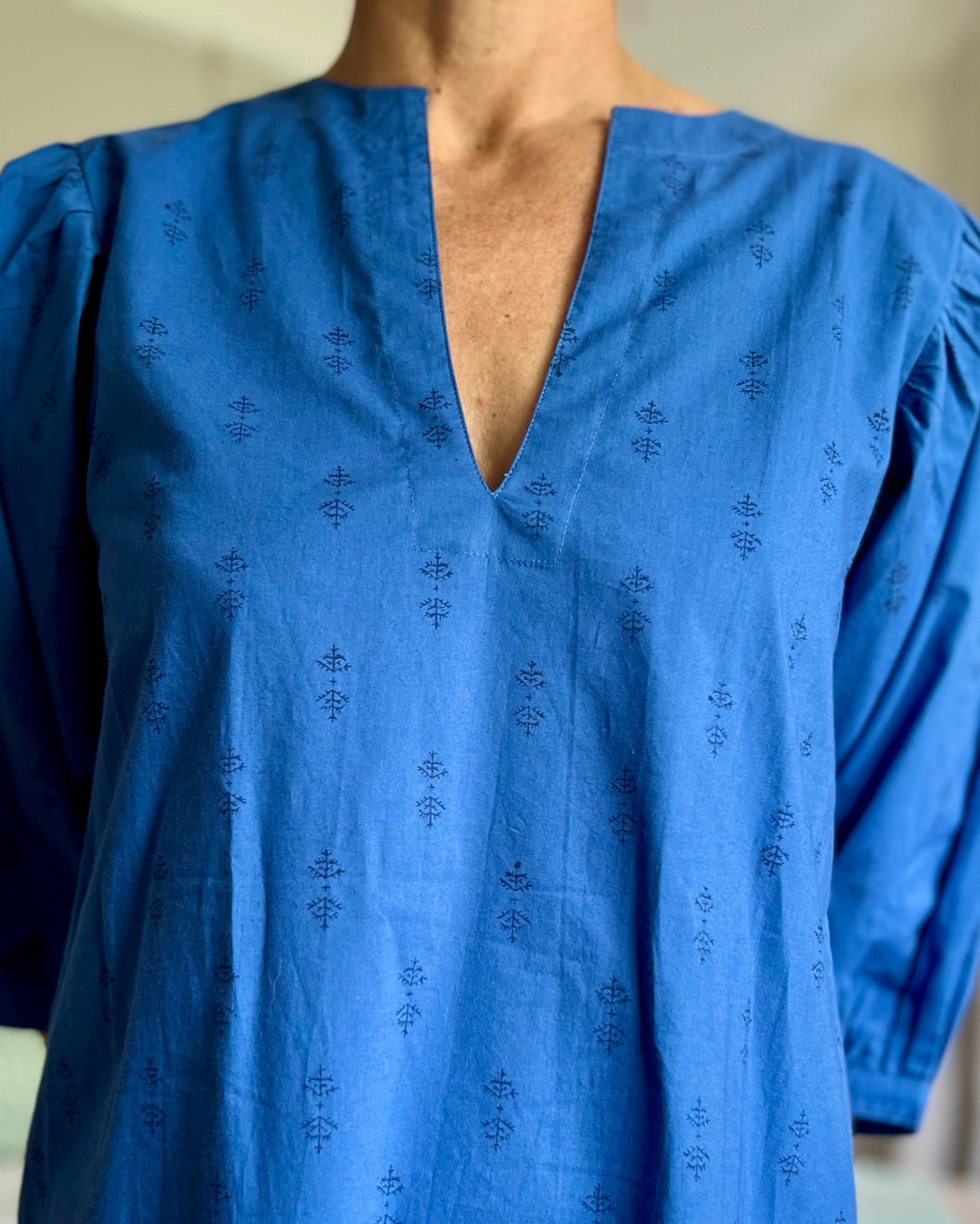 A woman standing in a room wearing a royal blue dress with puff sleeves and a V-neck