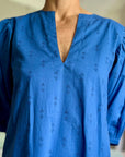 A woman standing in a room wearing a royal blue dress with puff sleeves and a V-neck