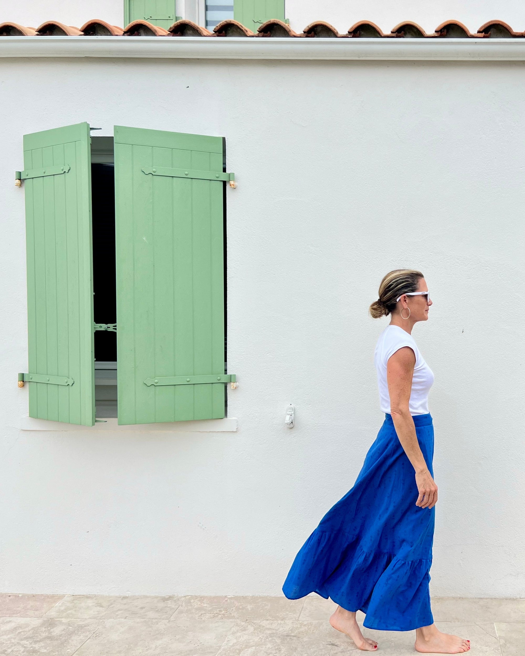 Woman in a royal blue hand block-printed maxi skirt standing in front of a white building with green shutters.