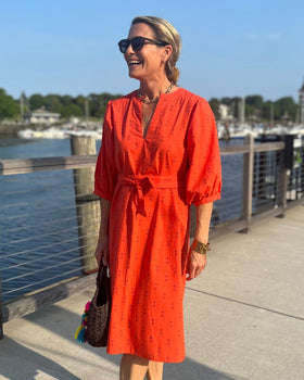 A person wearing a red dress with puff sleeves and sash belt next to water