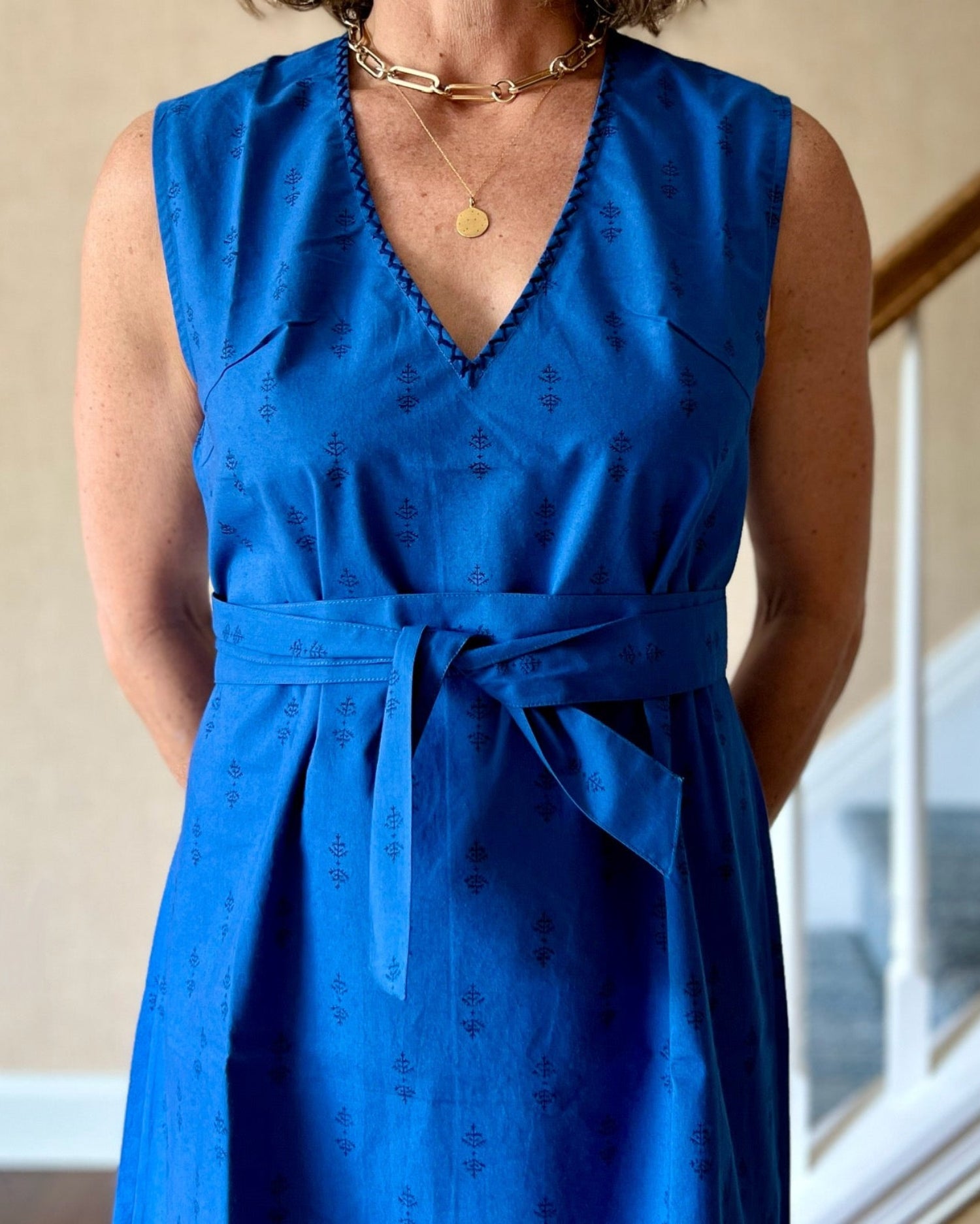 A woman wearing a sleeveless, trapeze-shaped royal blue mini dress with a deep v-neck, paired with a sash belt. 