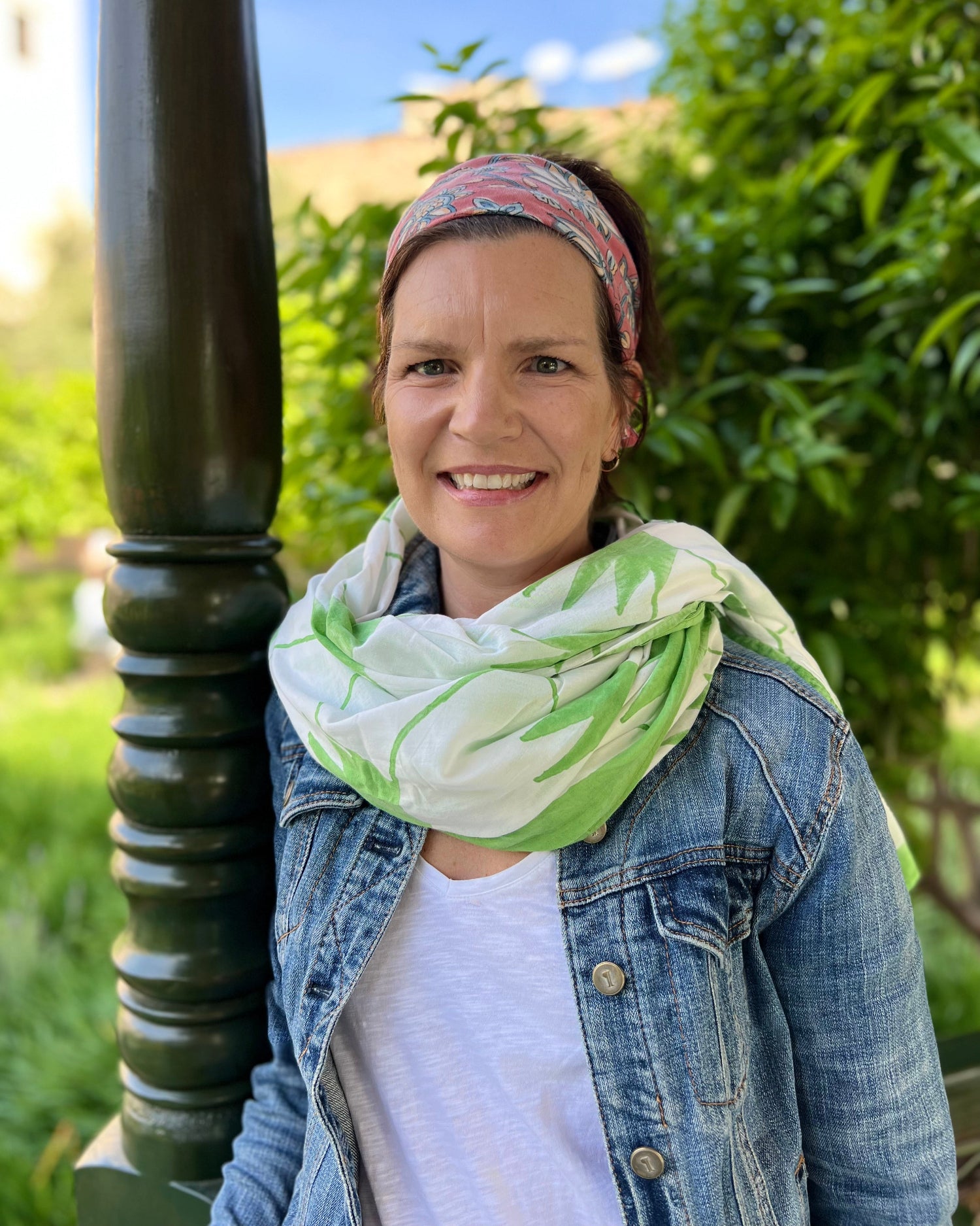 A person wearing a hand block-printed grass green and white sarong / grand scarf with green foliage in the background.