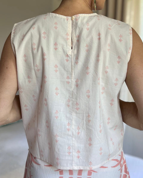 A person wearing a pale peach sleeveless boxy top with a crew neck and button closure at neck