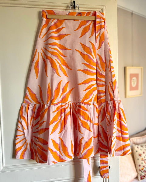 Pink and orange wrap skirt with ruffle on hanger on door