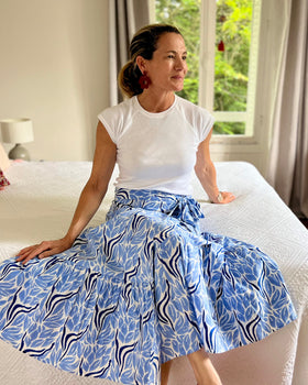 Woman sitting on a bed wearing a white top and blue and white hand block-printed wrap skirt in a bedroom.