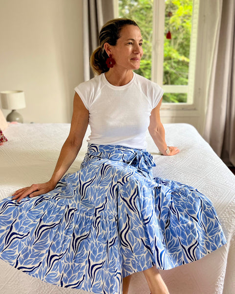 Woman sitting on a bed wearing a white top and blue and white hand block-printed wrap skirt in a bedroom.