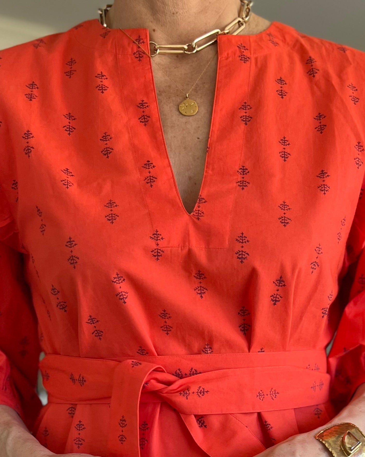 A person wearing a red dress with puff sleeves and gold jewelry