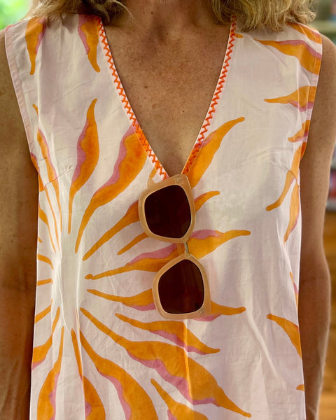 Close-up of pink and orange hand block-printed organic cotton dress with hand embroidery along the v-neck and sunglasses
