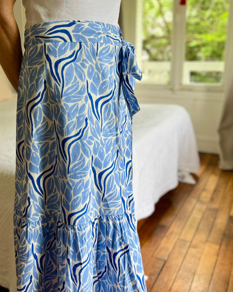 Woman wearing a white top and blue and white hand block-printed wrap skirt in a bedroom.