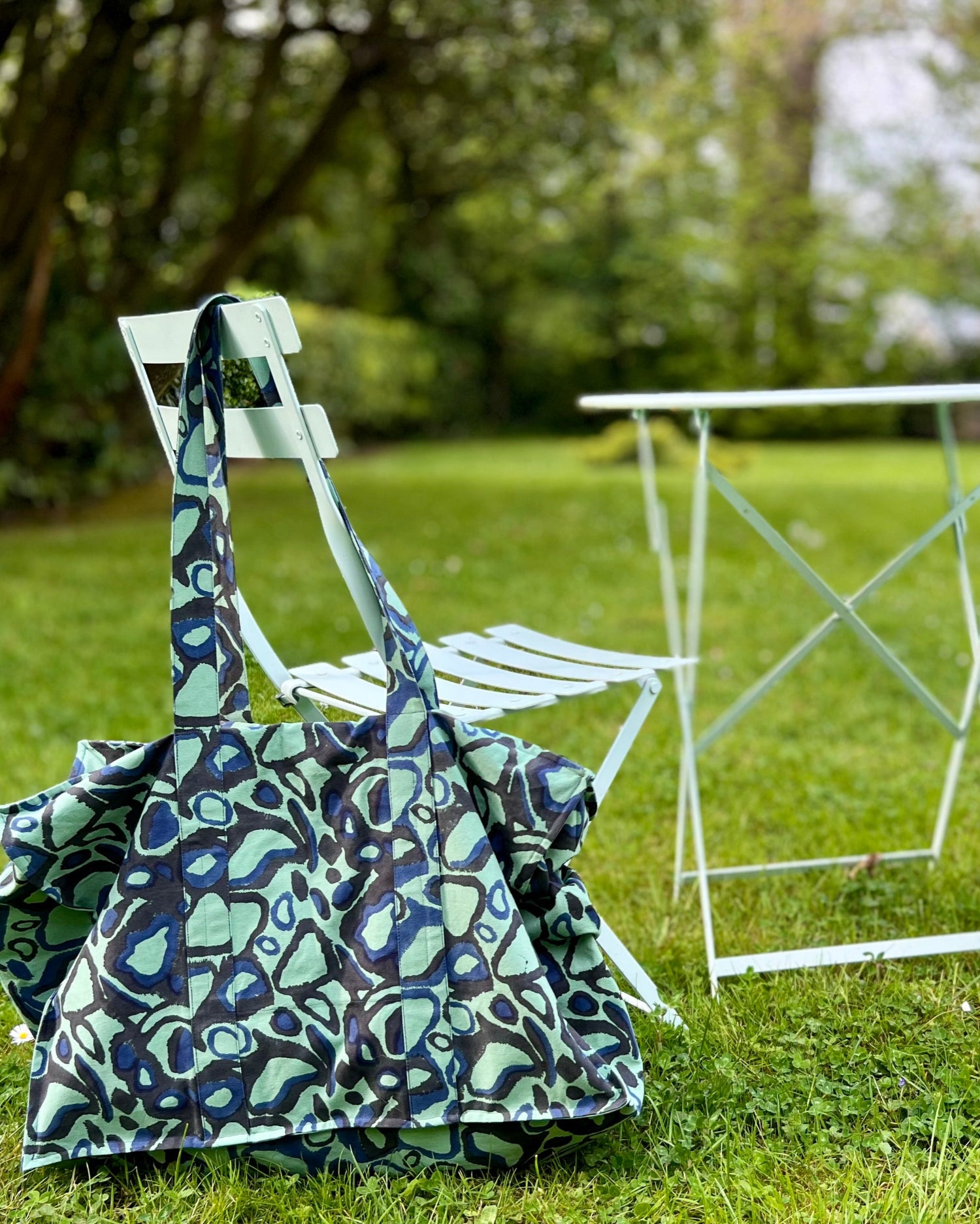 A green and black block printed tote bag with an animal print pattern hanging on a garden chair.